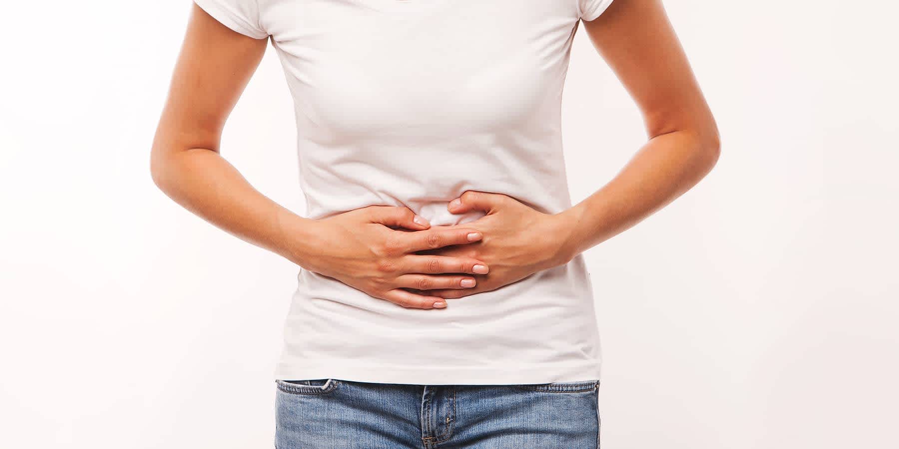 Woman in white shirt with her hands over her abdomen experiencing symptoms of untreated chlamydia