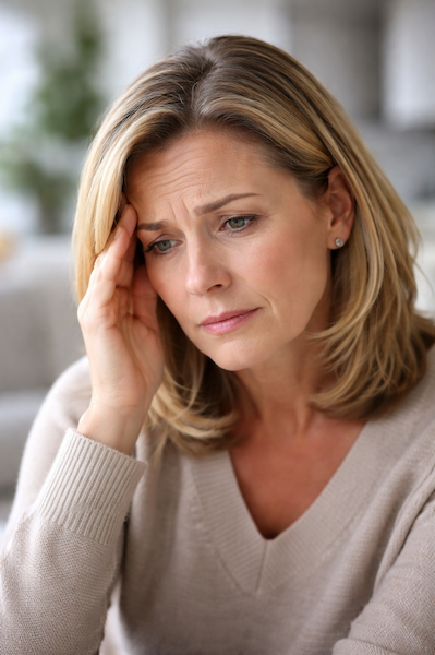 Middle-aged woman with a concerned expression, resting her hand against her temple in a quiet indoor setting