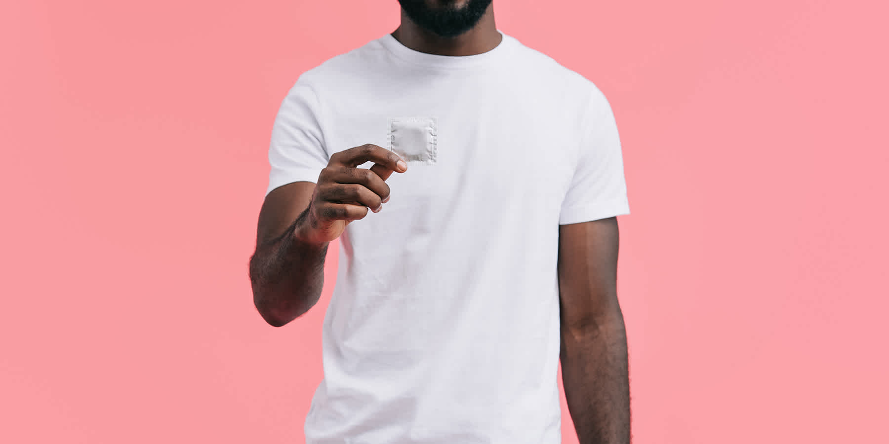 Man wearing white shirt and holding condom wrapper to represent men's sexual health
