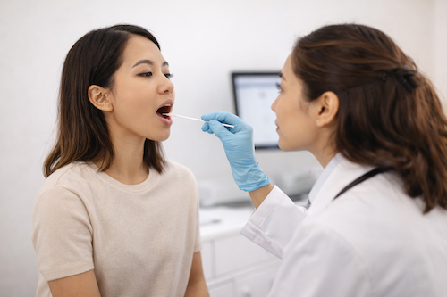 Healthcare provider collecting a throat swab sample from a patient during an STI test in a medical clinic setting.