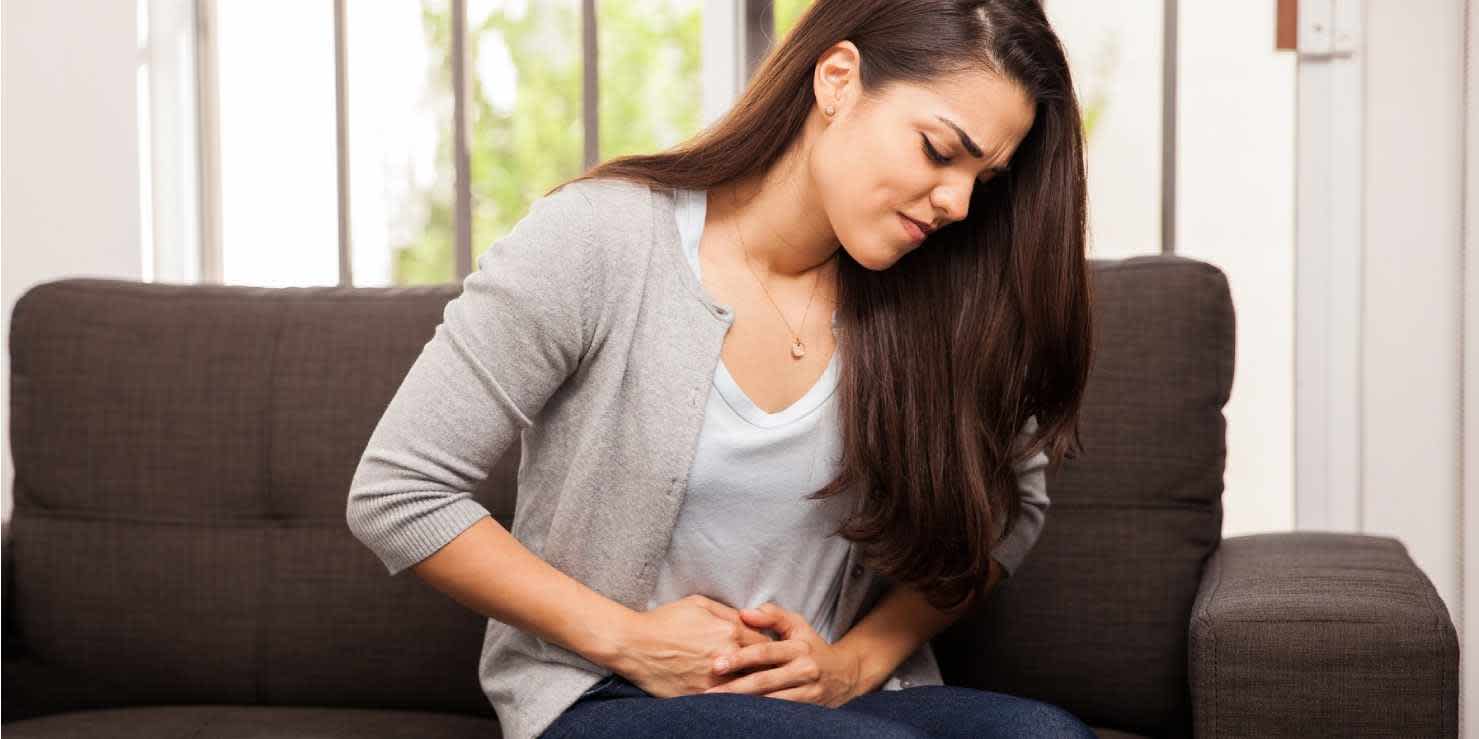 Woman sitting on couch and wondering about chlamydia in women while experiencing abdominal discomfort
