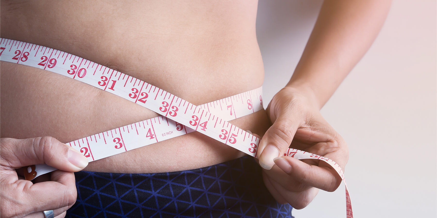 Woman measuring waistline while wondering about the symptoms of hormonal imbalance in women