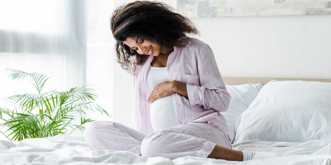 Pregnant woman in bed smiling and wondering about the effects of an STI on her unborn fetus