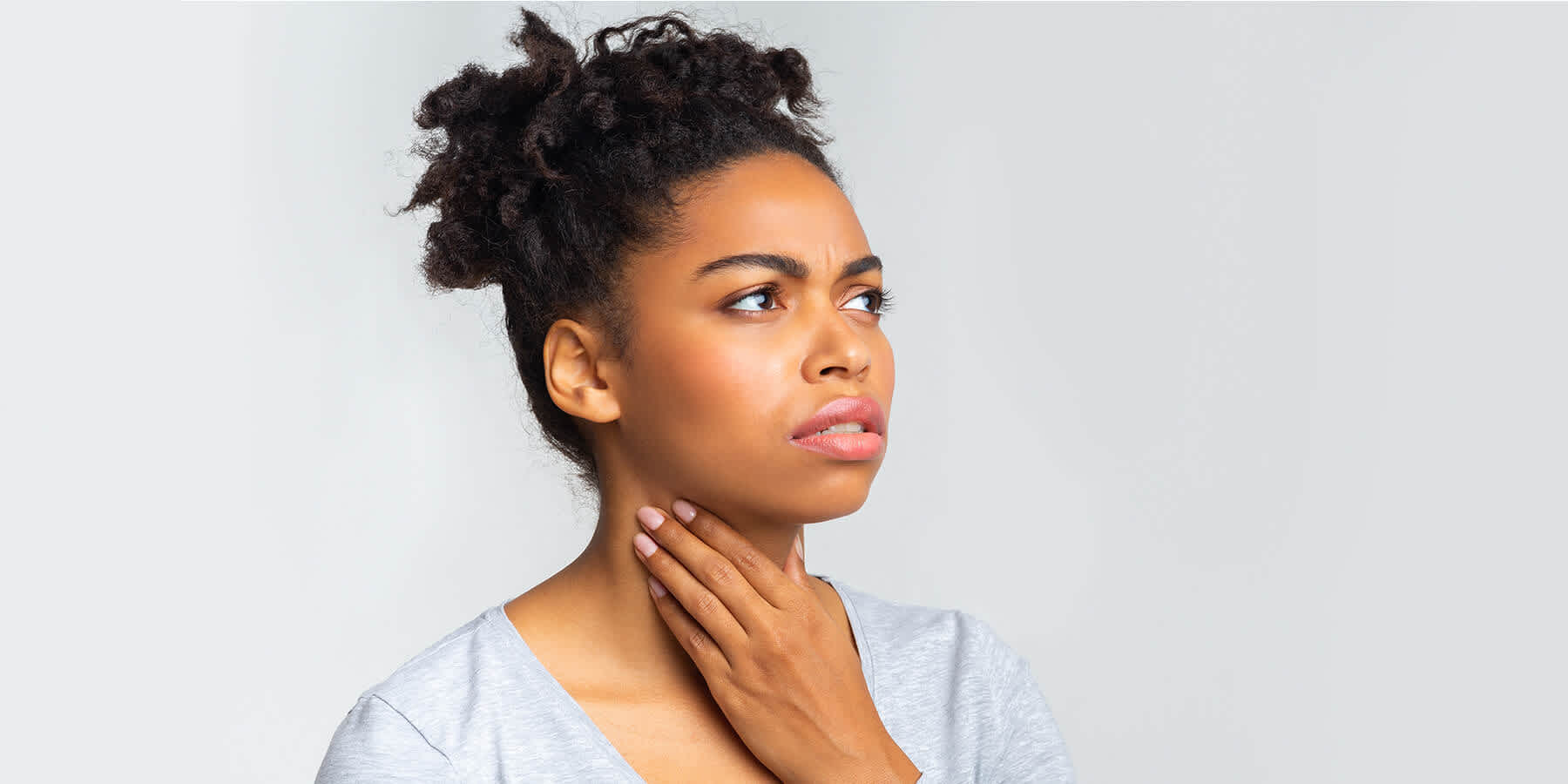 Young woman with hand on throat while wondering whether hypothyroidism is genetic