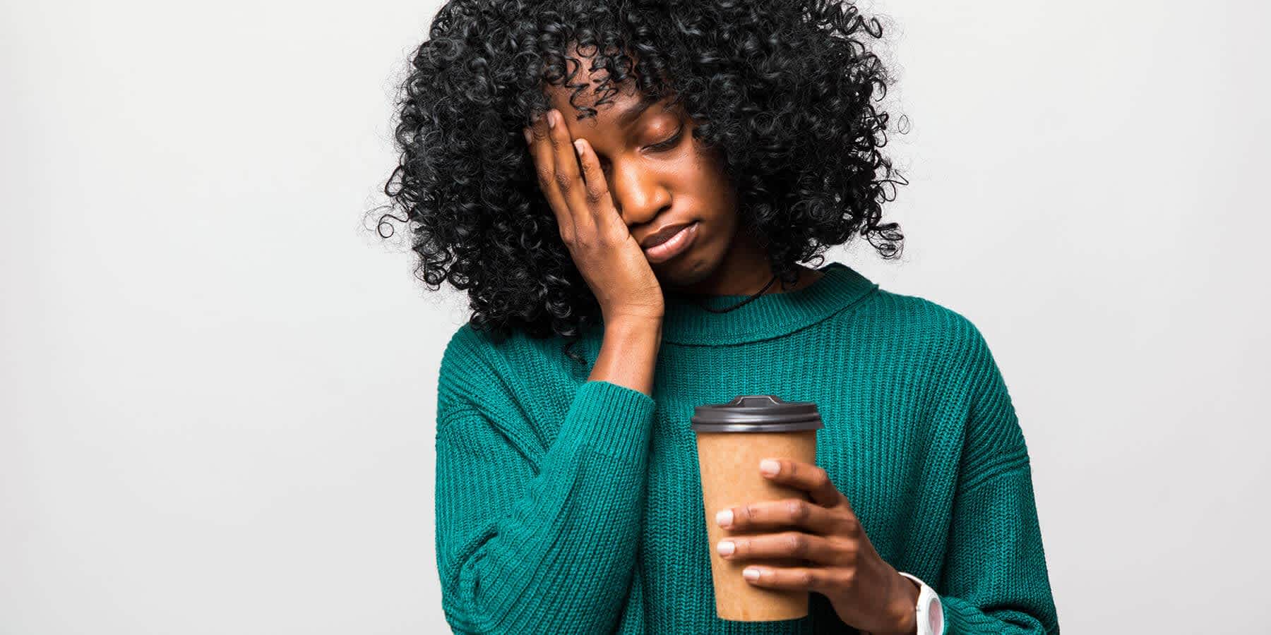 Tired woman with hand on face and holding coffee cup experiencing symptoms of hemochromatosis