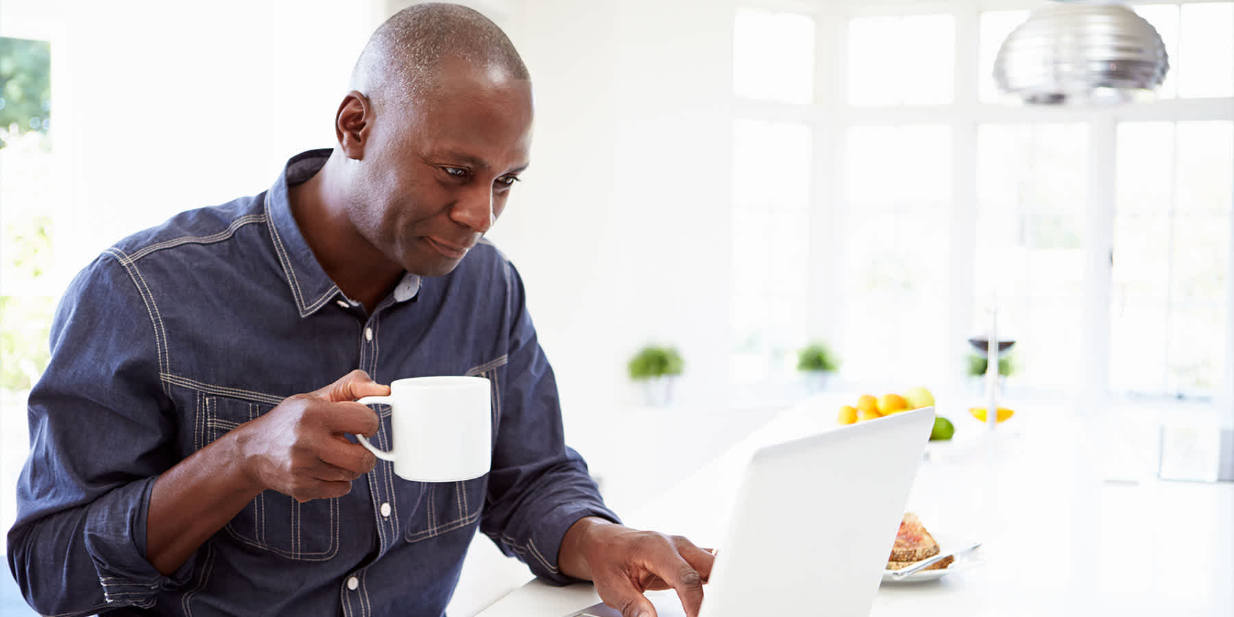 Man holding cup of coffee and using laptop to look up how to keep weight off after semaglutide