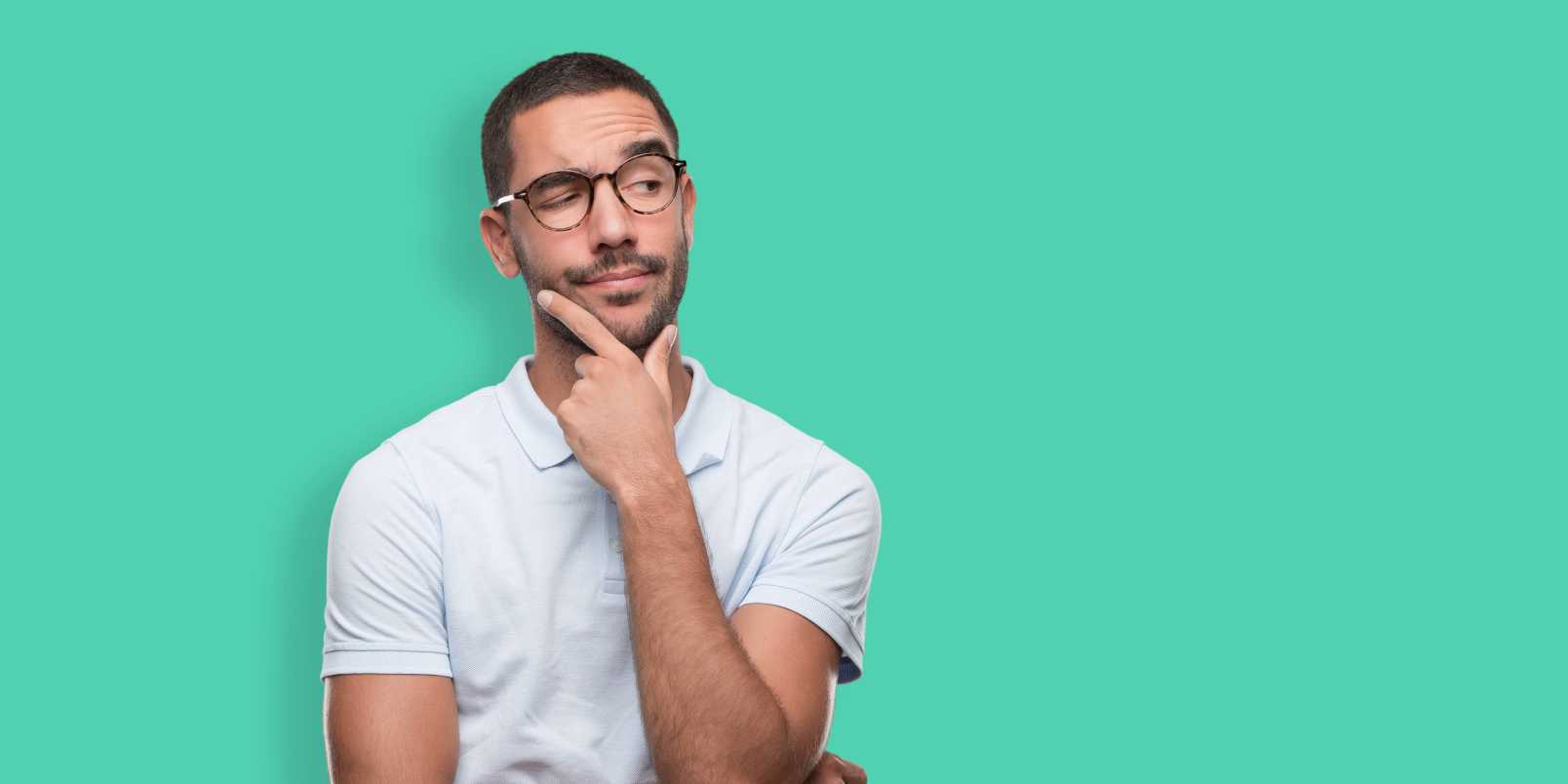 Man against a light teal background wearing glasses and stroking chin while wondering whether a vasectomy lowers testosterone