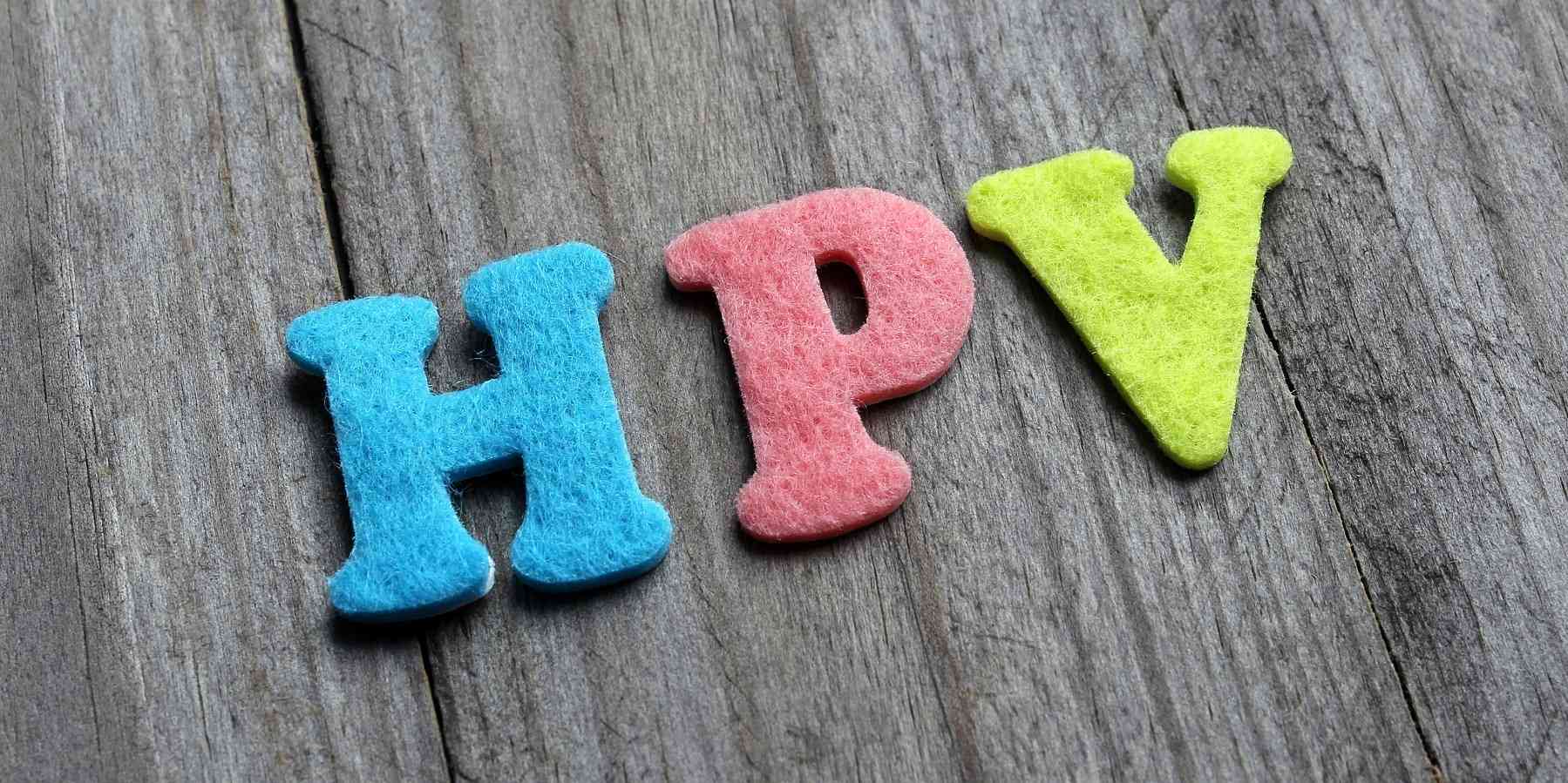 Multicolored cutout of the letters "HPV" against a wooden background