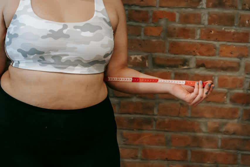 overweight woman in sports bra with measuring tape