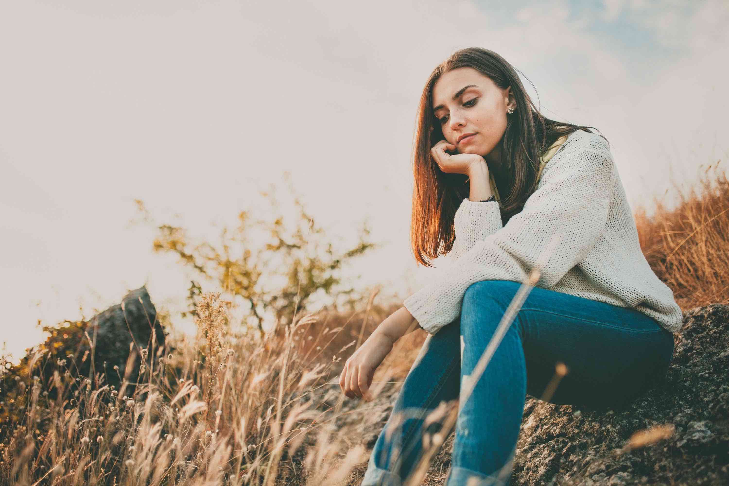 Young woman sitting on grassy hill while wondering, "Why do I have low mood?"