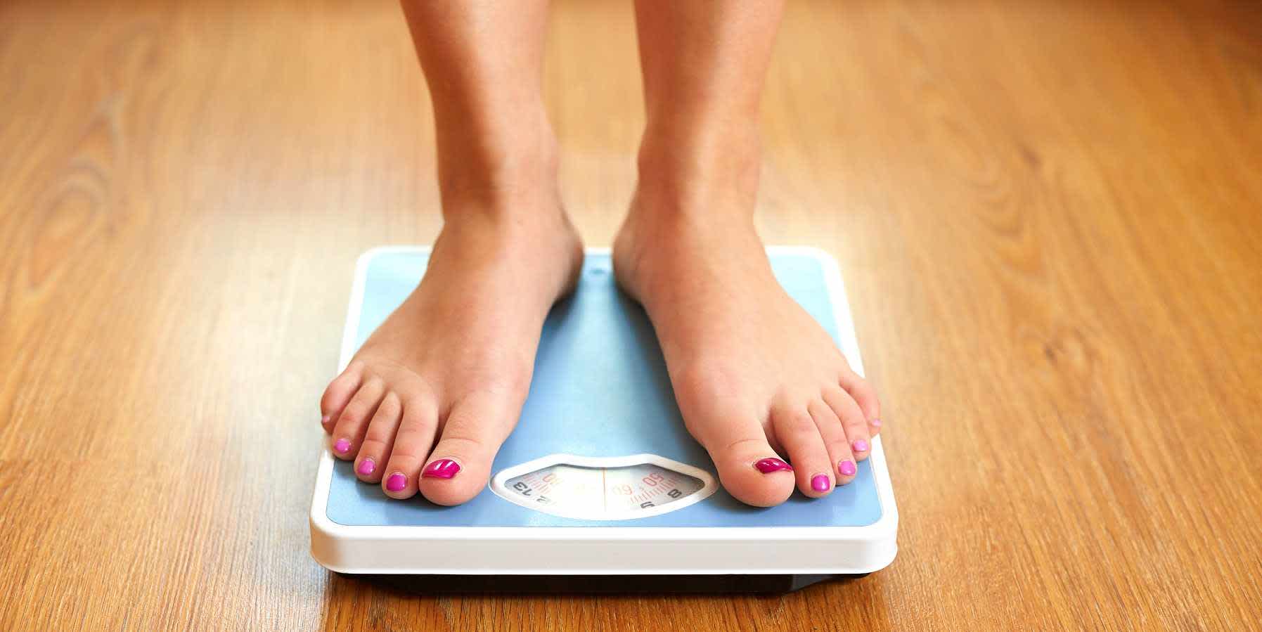 Woman stepping on bathroom scale while wondering whether estrogen makes you gain weight