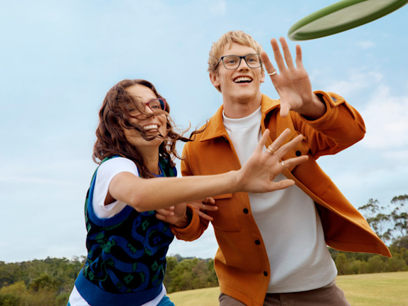 Young man and young woman smiling and about to catch a frisbee.