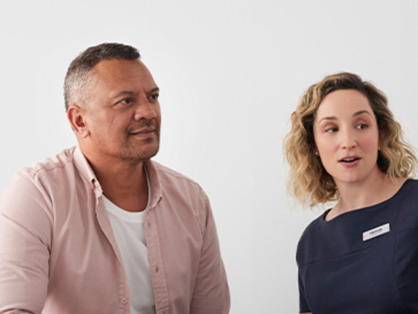 A woman gestures towards a computer screen while a man looks on attentively.