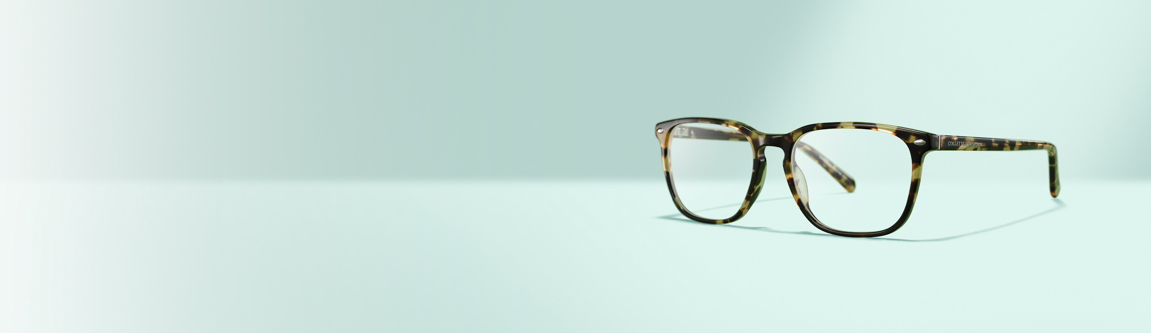 A pair of tortoiseshell eyeglasses with rectangular frames is displayed on a light blue surface with a light blue background.