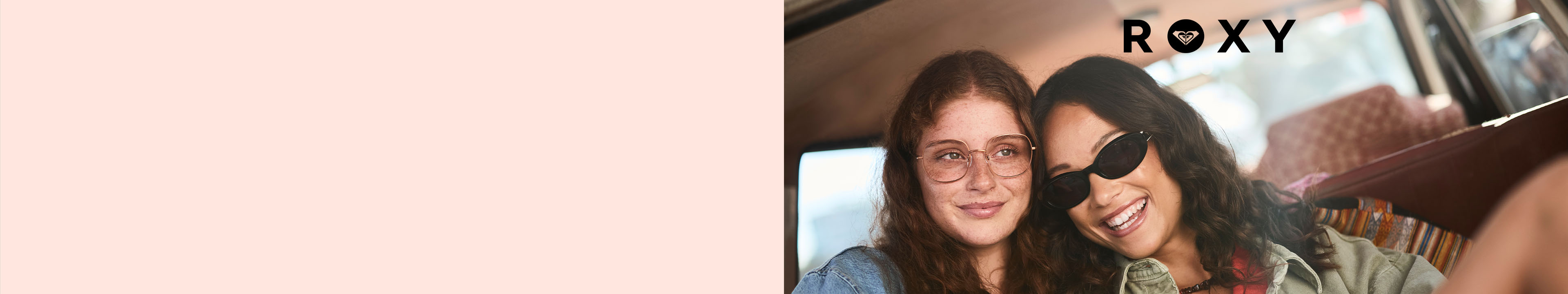 Two women wearing Roxy sunglasses and casual attire smile while sitting together in a vehicle. The brand "ROXY" is elegantly displayed above them.