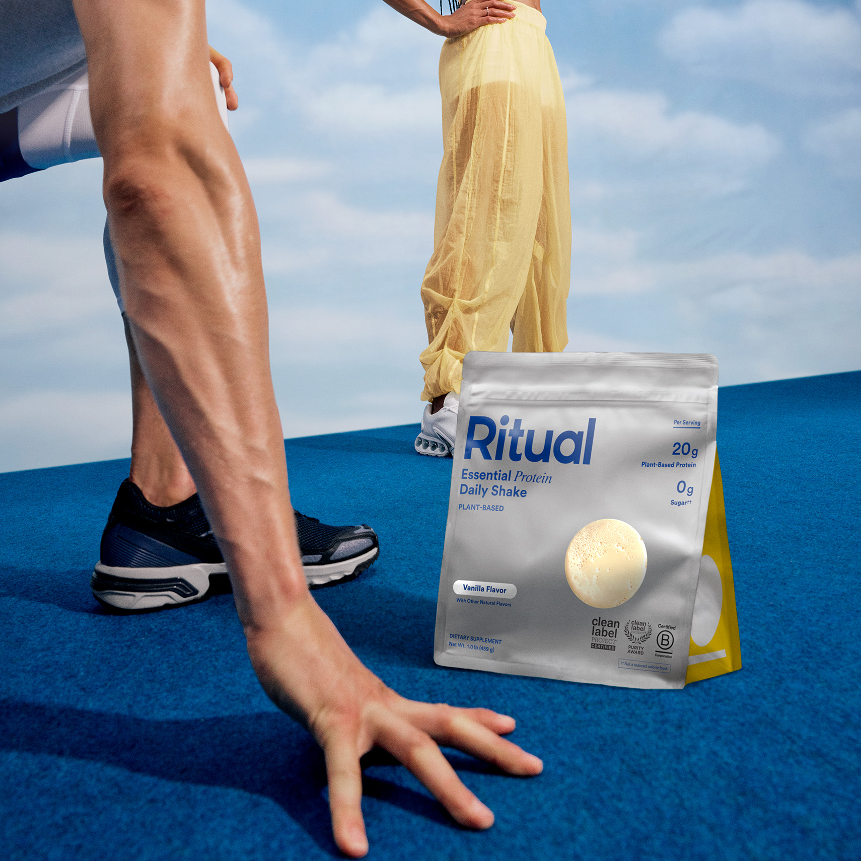 Two models posing around a bag of Essential Protein Daily Shake with a blue floor and a sky in the background.