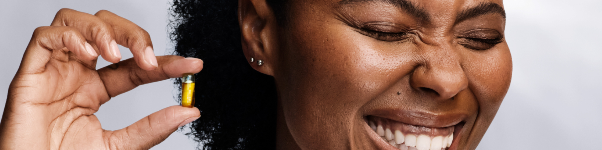 Woman holding a HyaCera capsule while smiling and scrunching her nose.