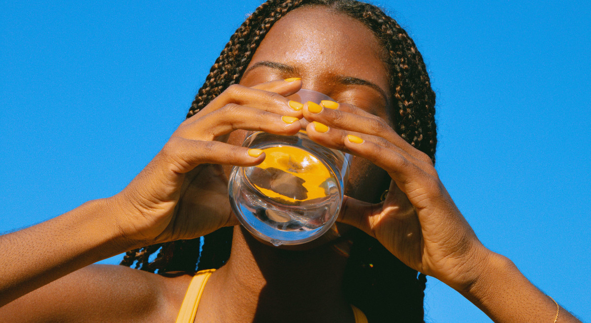 Model drinking a glass of water with a blue background.