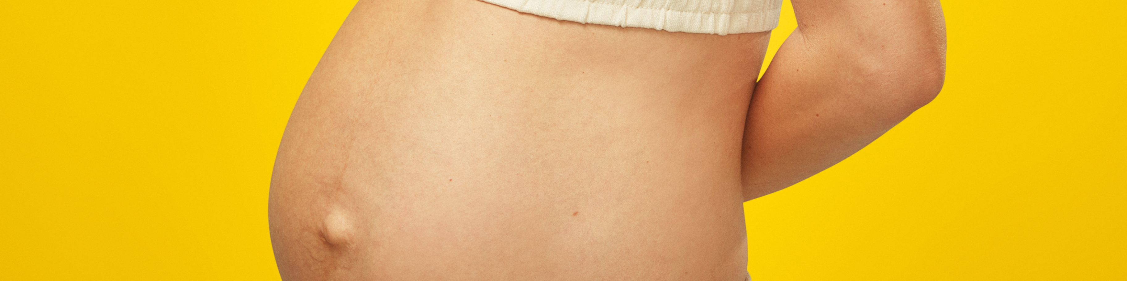 Pregnant bump in front of a yellow background.