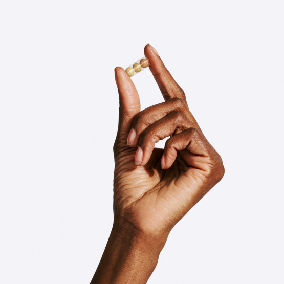 A model's hand holding a Stress Relief capsule on a grey background