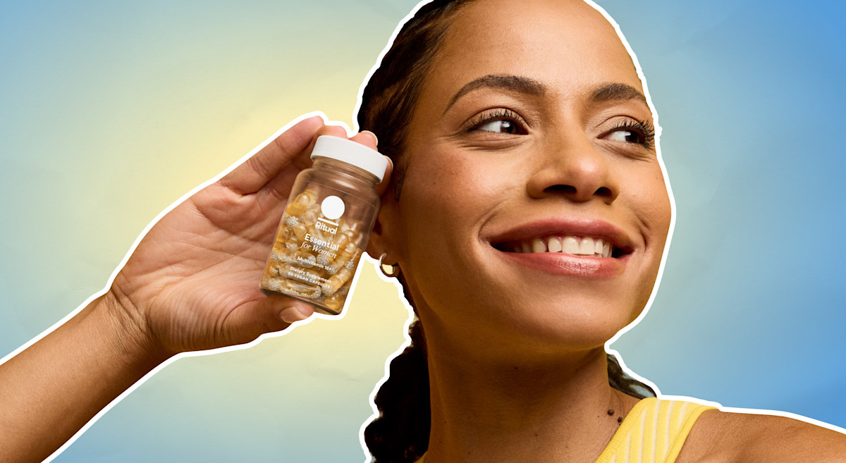 Woman holding bottle of vitamins up to face on a blue and yellow gradient background.