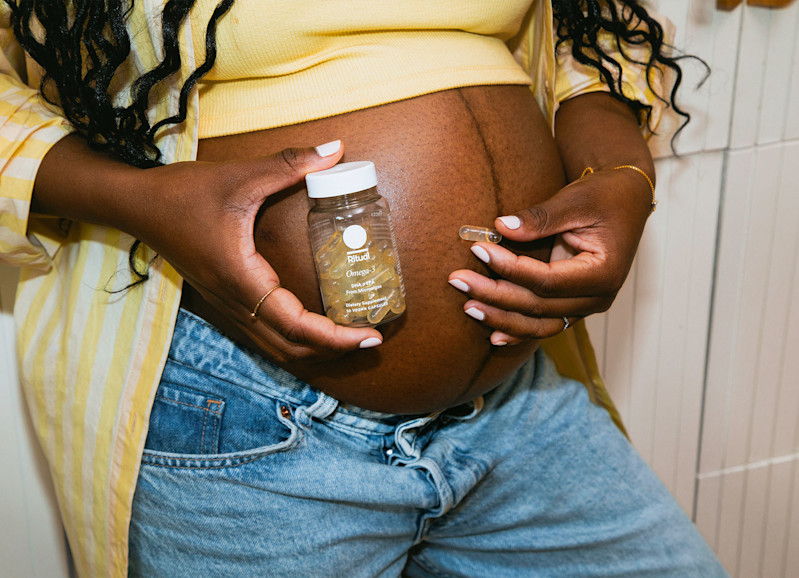 Pregnant model holding a capsule and bottle of Omega-3 DHA & EPA in front of her belly.
