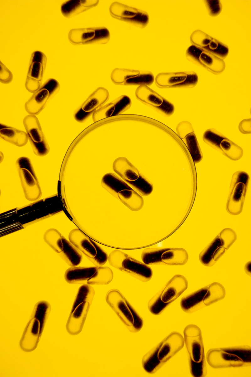 Magnifying Glass over Essential Prenatal Pills with a yellow background.