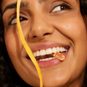 A model with an Omega-3 DHA & EPA capsule in their mouth with a decorative lemon rind in frame.