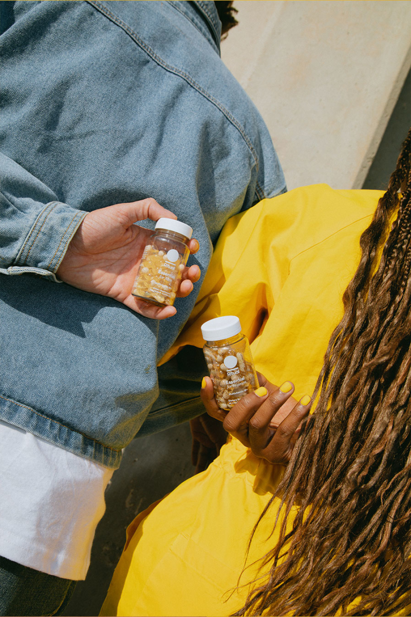 Two models holding Ritual multivitamin bottles, one is in a yellow shirt and the other is in a denim jacket.
