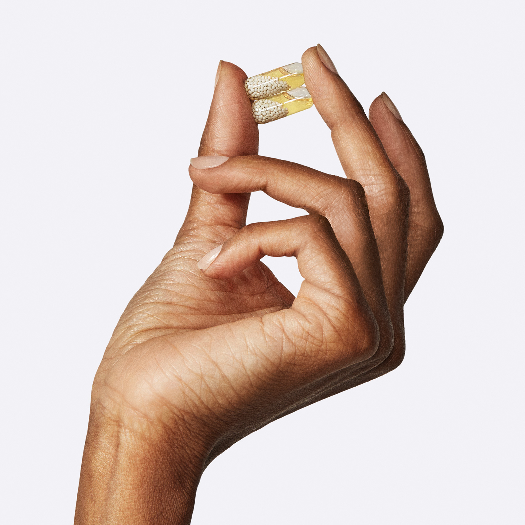 Closeup shot of a woman's hand holding 2 Ritual's Essential for Women 50+ capsules