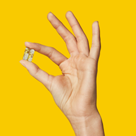 Closeup image of a teen model holding 2 Essential for Teen (Hers) pills in hand