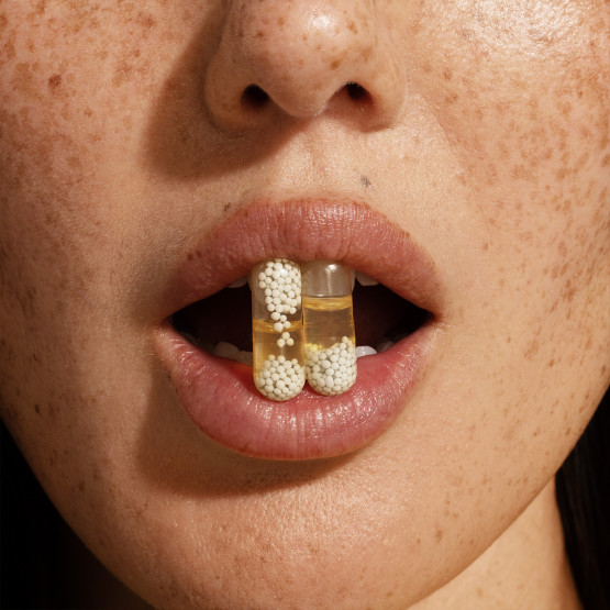 Closeup image of woman holding 2 Essential for Women 18+ pills in her lips
