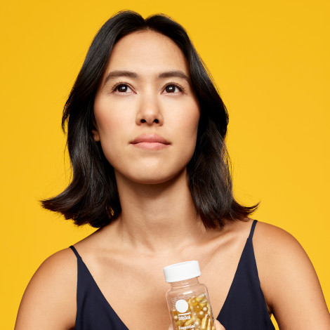 Woman holding Ritual's Essential Postnatal bottle with yellow background