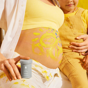 Pregnant model and toddler sit together while the model holds a bottle of Natal Choline