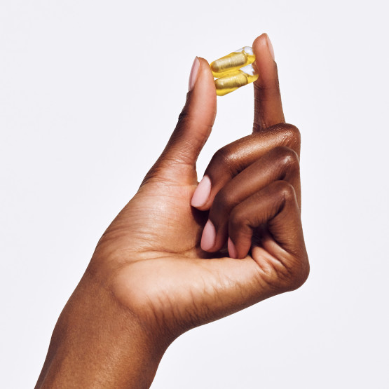 Closeup shot of woman holding 2 Ritual Essential Postnatal pills in hand