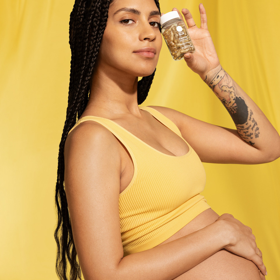 Woman holding prenatal vitamins while putting her hand over her belly.