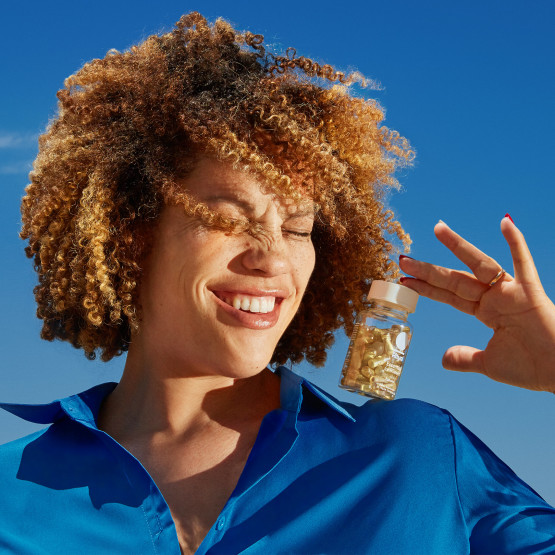 Woman holding Ritual's Essential Postnatal bottle with blue sky background