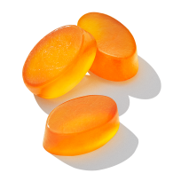 Close up image of three (3) Essential for Kids 4+ multivitamin gummies. They are oval and orange in color. 