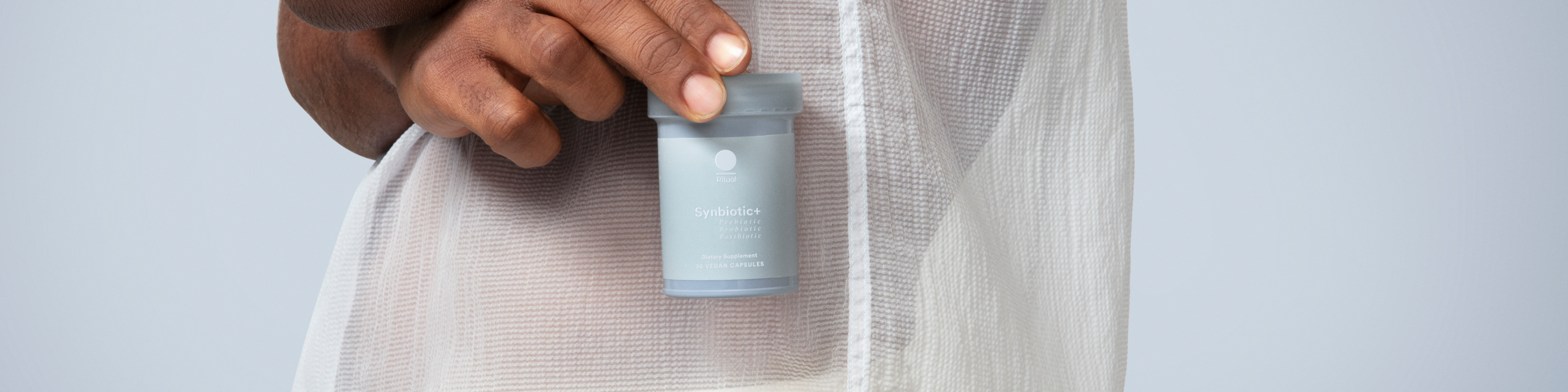 Man holding a light blue Synbiotic+ Ritual probiotic bottle. 