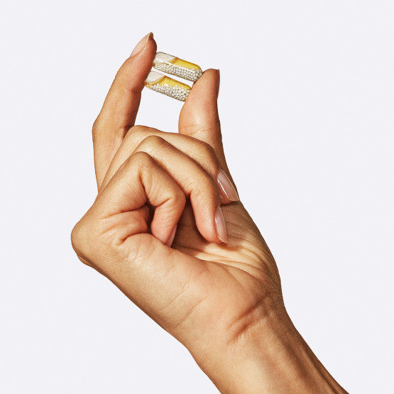 Closeup image of woman holding 2 Essential for Women 18+ pills in her hand