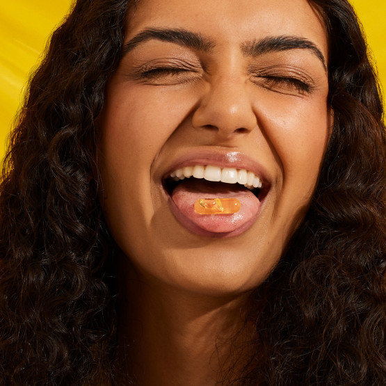 A model with an Omega-3 DHA & EPA capsule on their tongue.