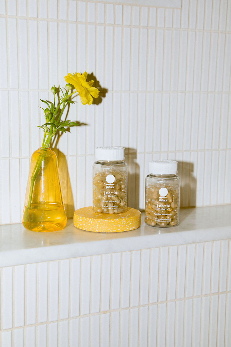 Bottles of Prenatal and Postnatal Multivitamins next to a vase with a yellow flower.