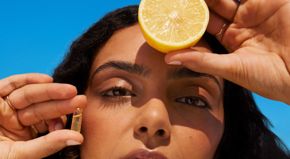 Model posing with a Ritual Omega-3 capsule and half a lemon in front of her face with a blue background.