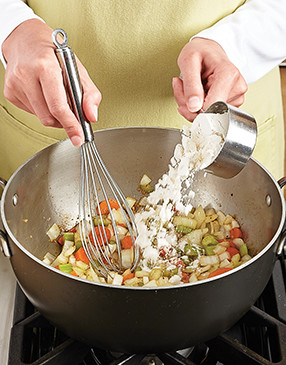 Adding flour to the drippings and vegetables coats them and forms a roux to thicken the soup.