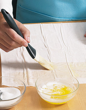 Lightly butter a sheet of phyllo dough and sprinkle it with sugar before rolling it into a loose tube.