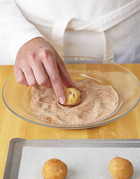 Roll balls of dough in spiced sugar to coat, then place them in rows on a lined cookie sheet.