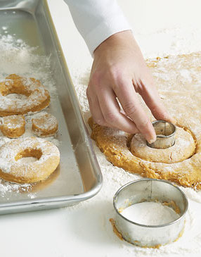 Round biscuits cutters are great for cutting doughnuts, but for even easier work use a specialized doughnut cutter dipped in flour.