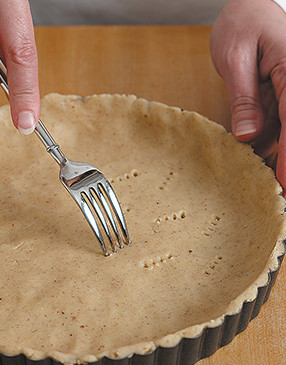 To prevent the crust from puffing during baking, dock it by poking holes in it with a fork.