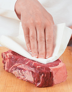 Blotting the steak's surface allows the seasonings to adhere and ensures a better sear on the grill.