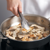Use a pair of tongs to turn and separate the Cajun-seasoned chicken pieces as they saut&eacute; in the pan.